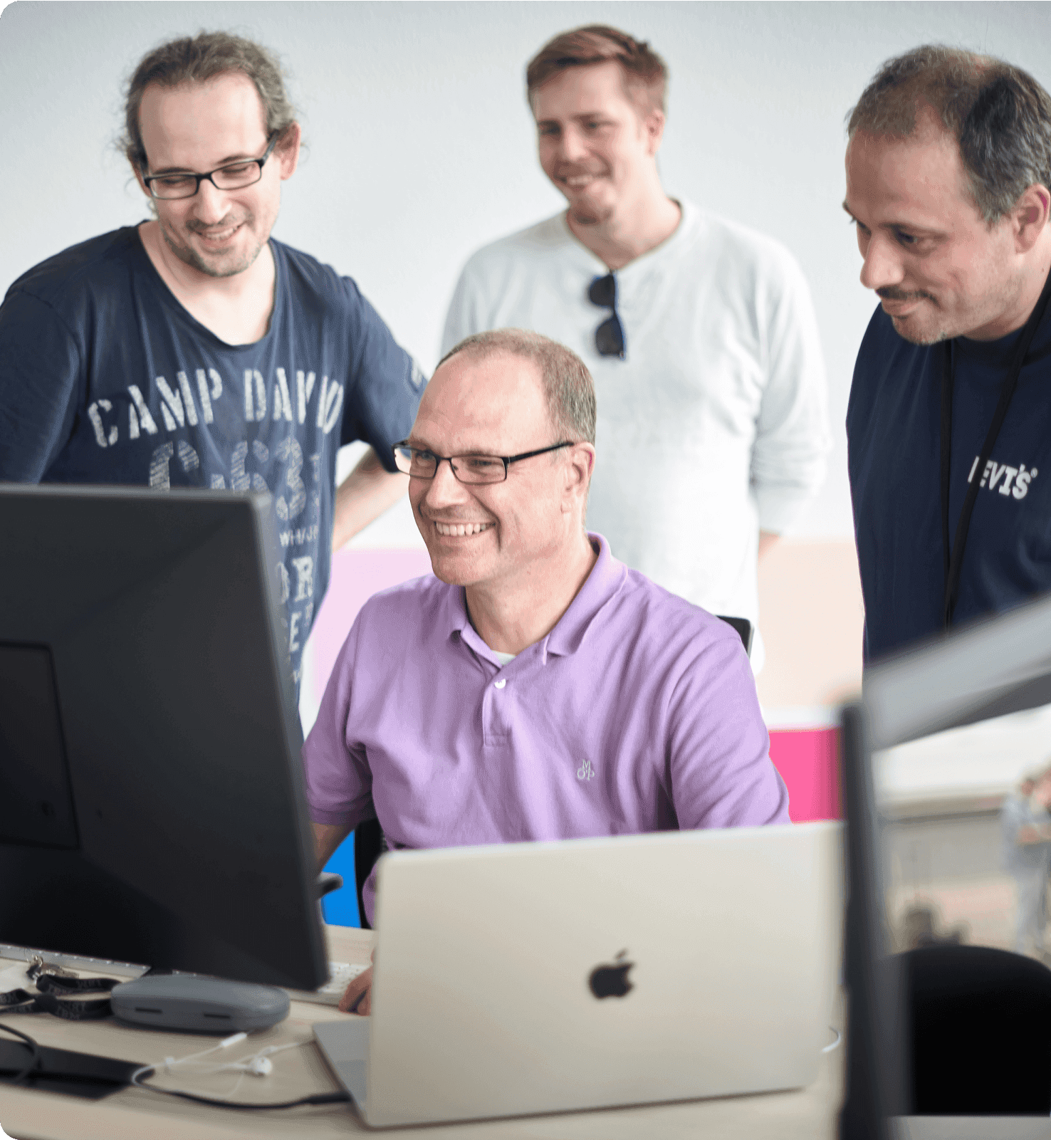 Ein Mitarbeiter sitzend am Laptop und 3 weitere stehen drum herum