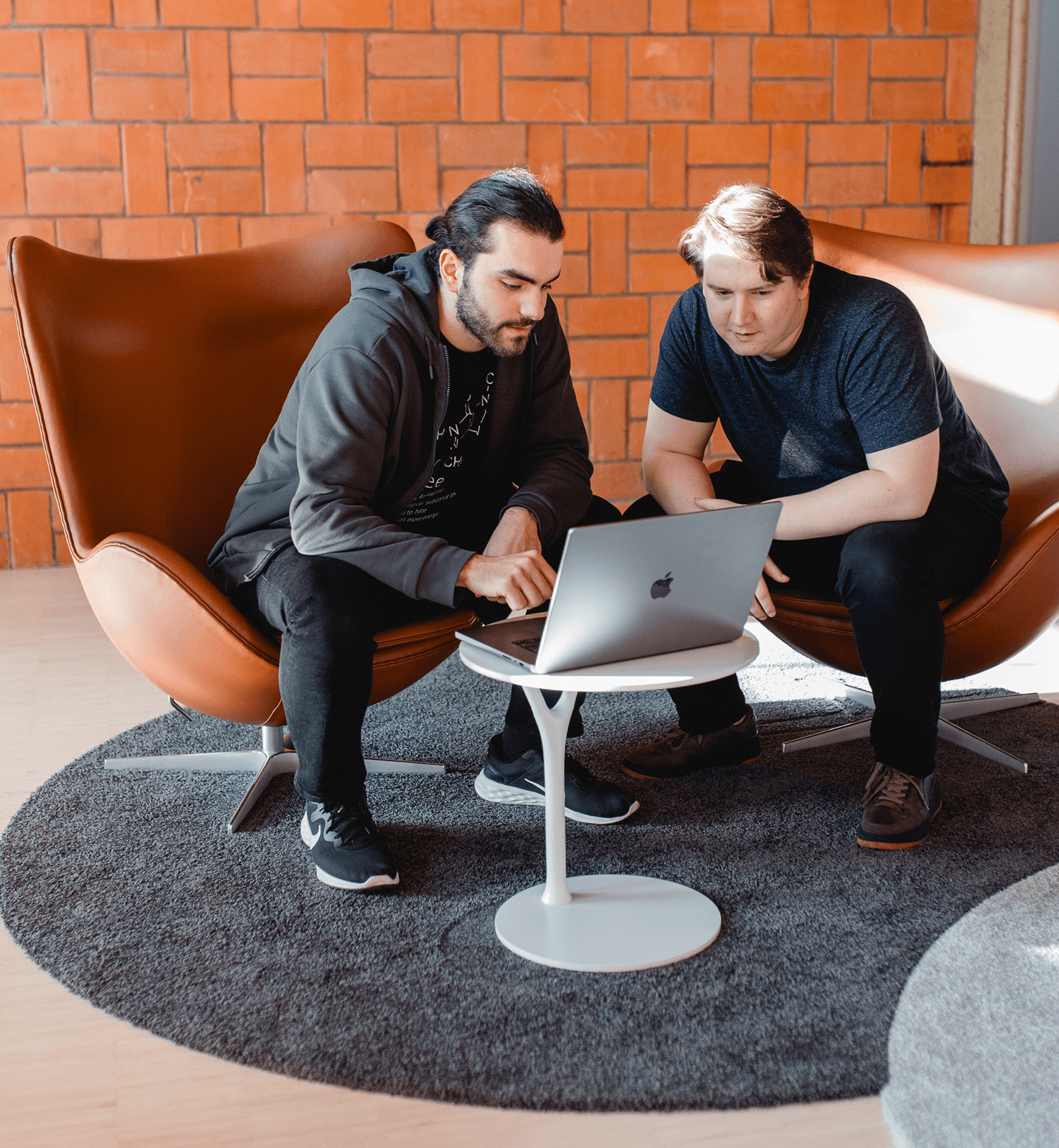 Zwei Mitarbeiter vor einem Macbook in Sesseln sitzend